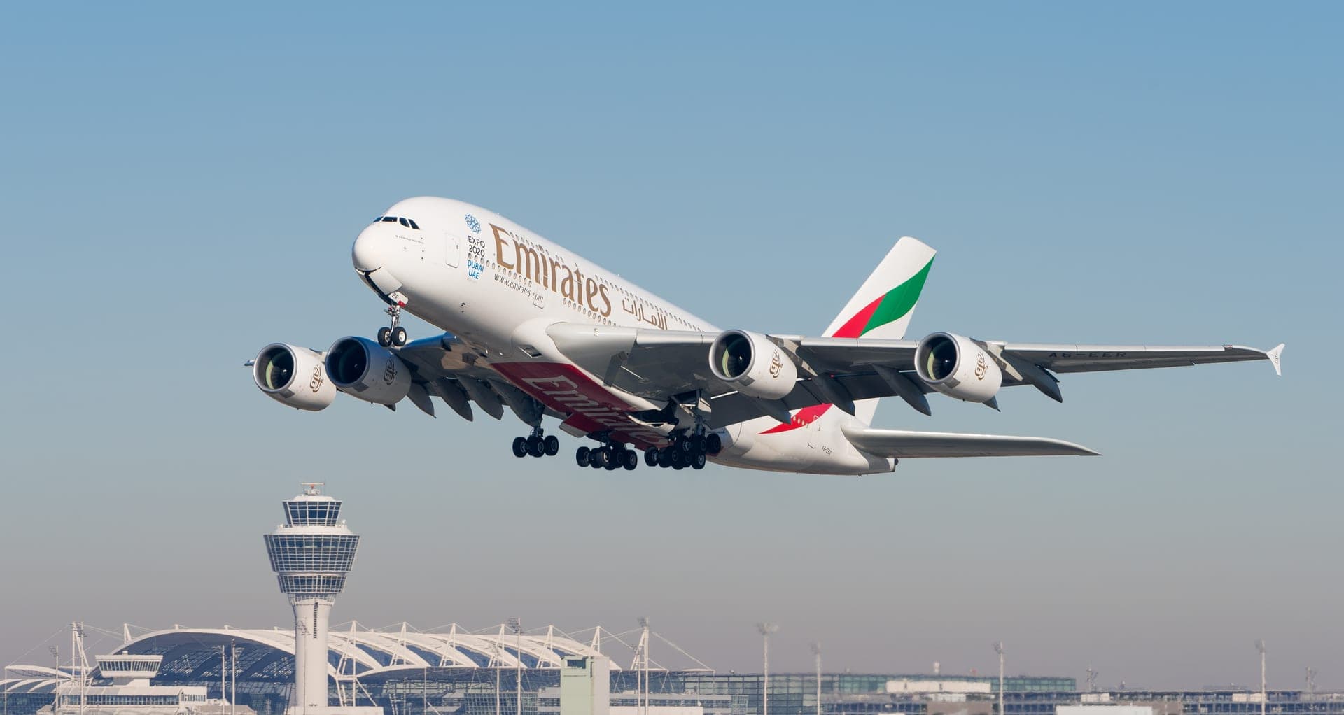 An Emirates Airbus A380-861 climbing away from Munich Airport, all four engines visible beneath the full-length double-deck fuselage
