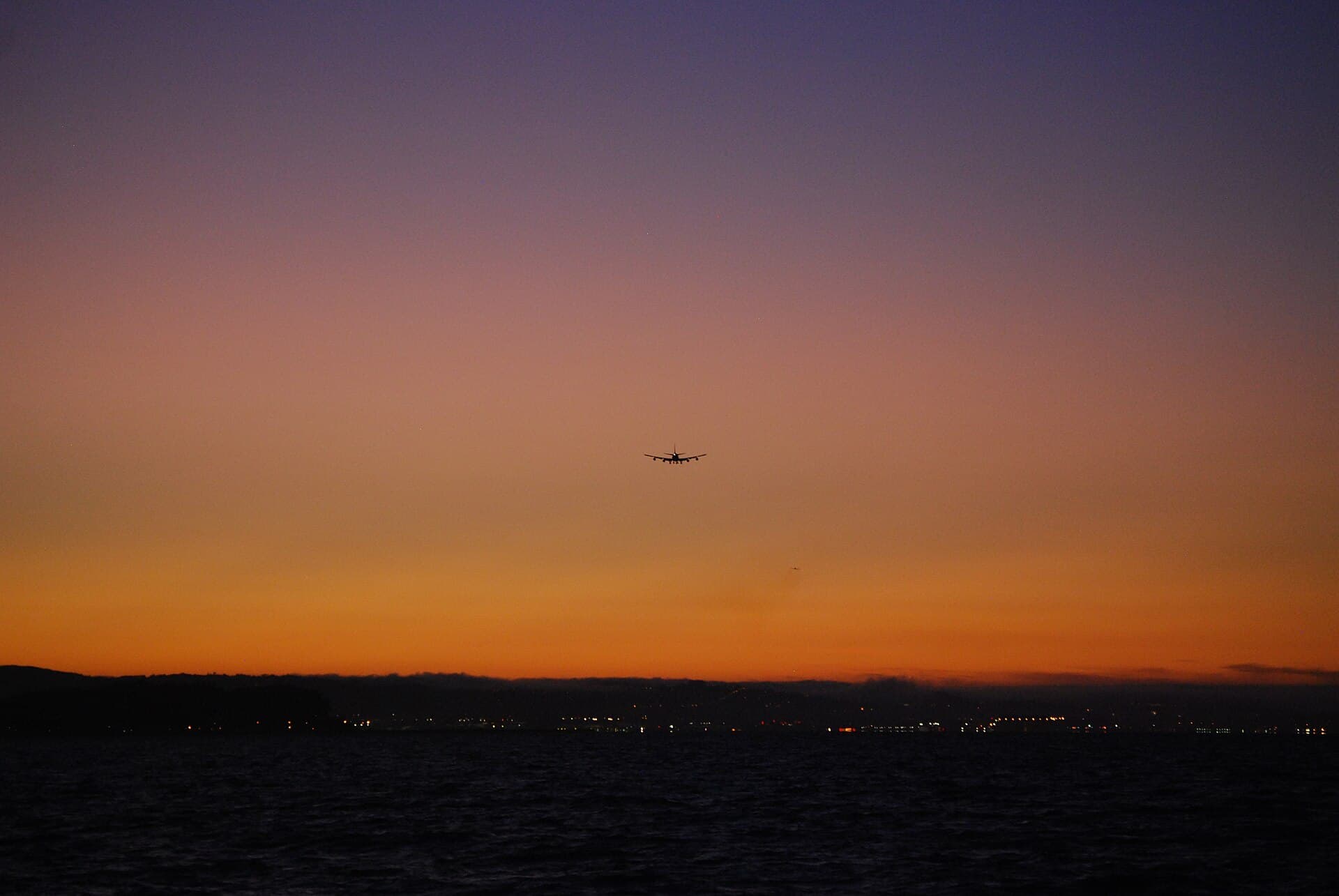 A Boeing 747-400 banking in warm evening light, its raked wingtips and winglet catching the sun