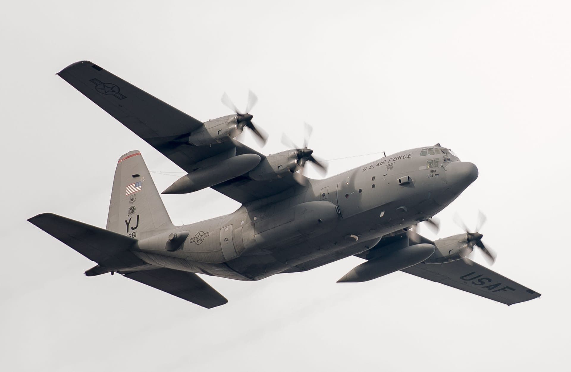 A U.S. Air Force C-130 Hercules of the 36th Airlift Squadron banking in flight over Yokota Air Base, Japan, seen from ahead and to the side with its high wing, four turboprops and upswept tail clearly visible