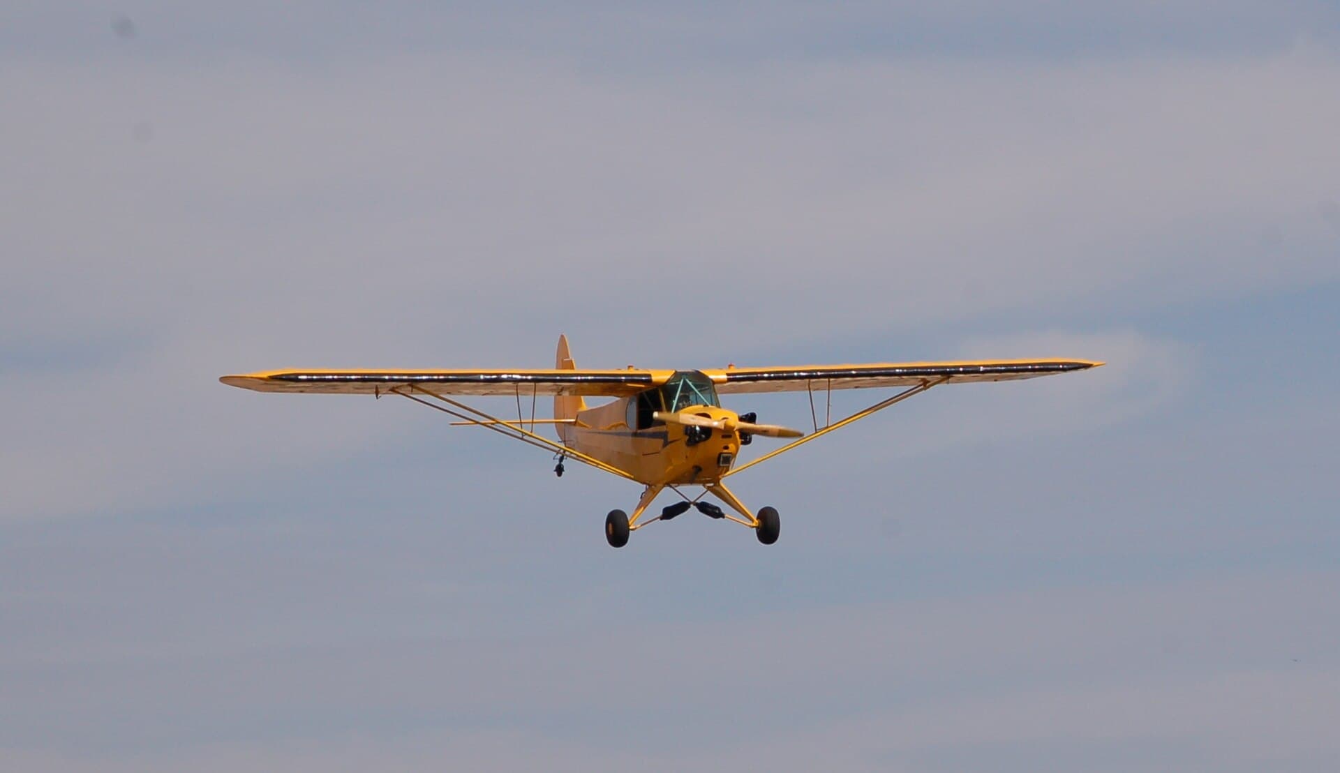 A yellow Piper J-3 Cub in flight against an overcast sky