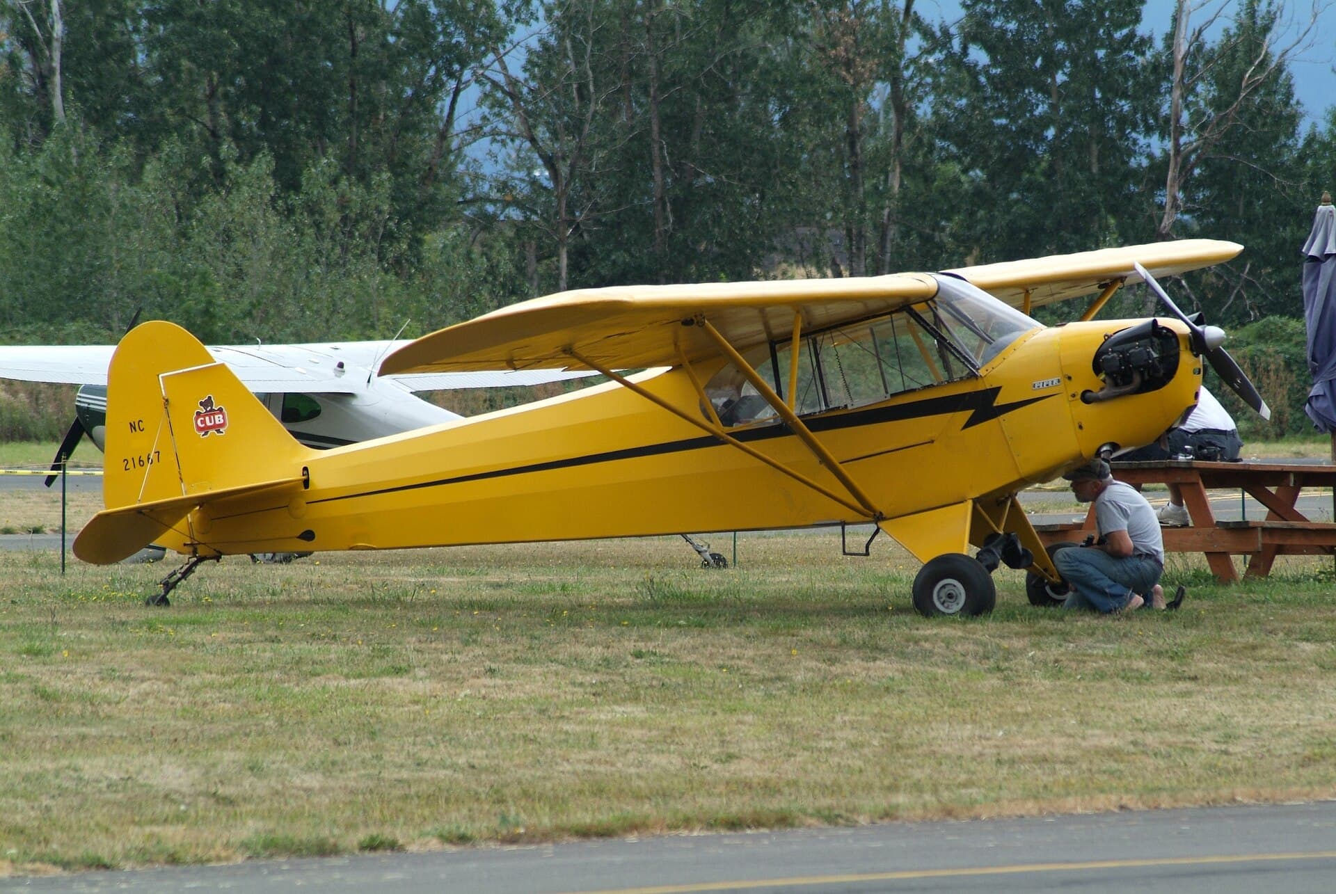 A yellow Piper J-3 Cub with black lightning-bolt trim parked on grass