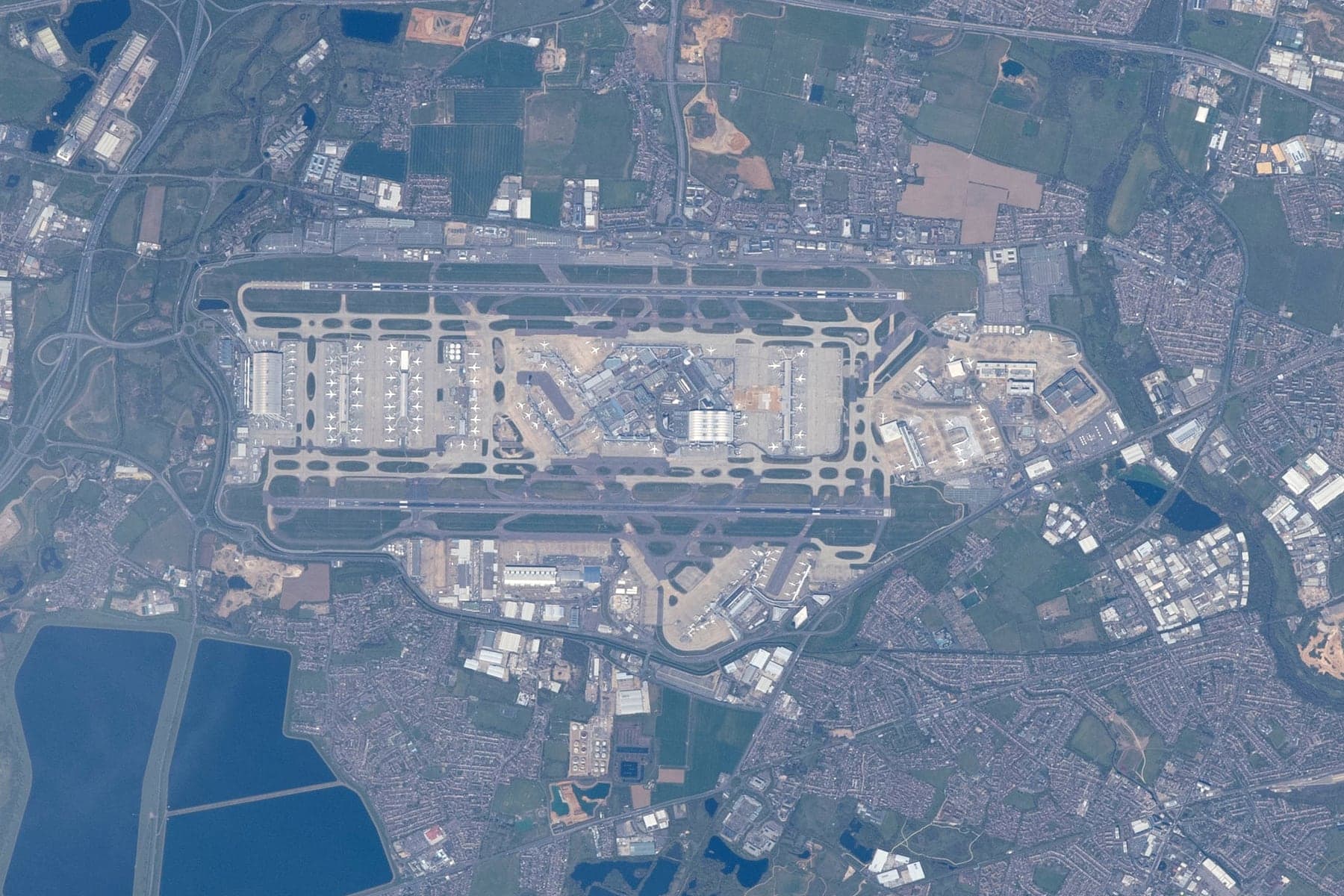Vertical colour photograph of Heathrow taken from the International Space Station in April 2021: the two parallel east-west runways with the central terminal area between them, Terminal 5 at the western end and the cargo area to the south and Terminal 4 to the south-east, surrounded by west London suburbs and, to the west and south-west, the reservoirs of the Colne Valley
