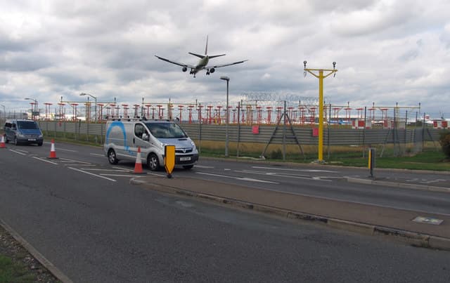 An airliner on short final for runway 27L over the approach lighting and the airport's northern perimeter road
