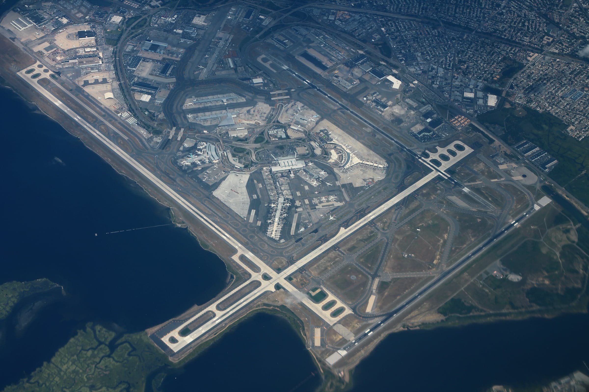 The whole airport from the air in 2016: the central terminal ring inside its road loop, the long runway pairs crossing at right angles, and Jamaica Bay on three sides