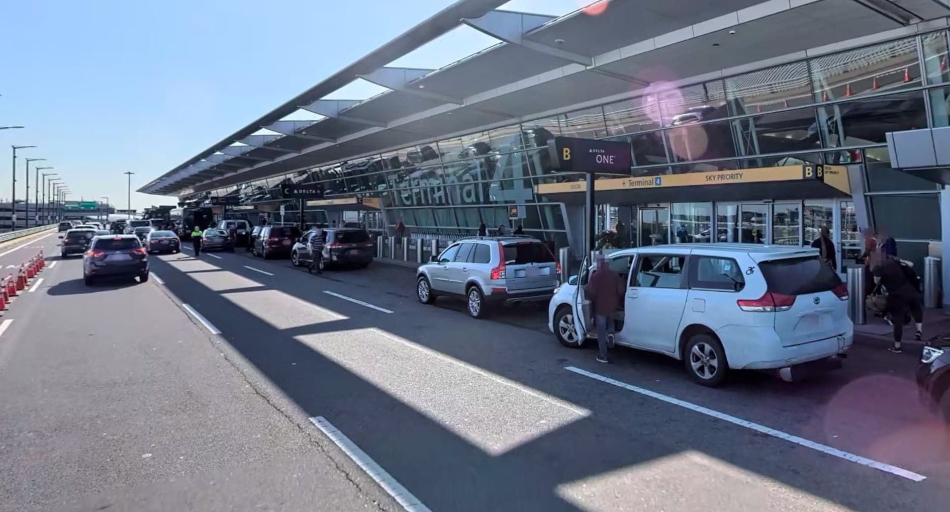 The departures roadway of Terminal 4 in June 2019, cars at the kerb under the terminal's long glazed canopy