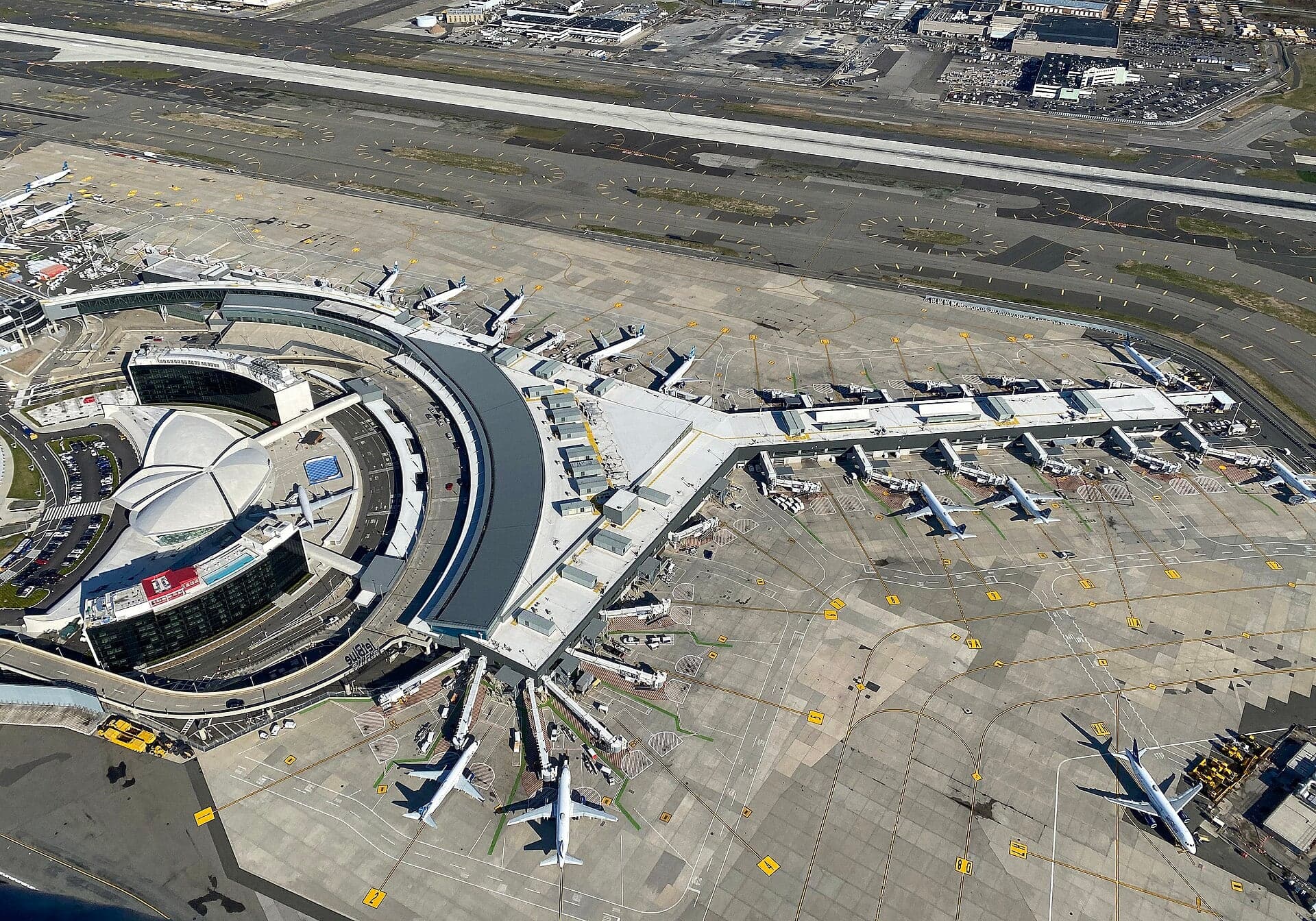 JetBlue's Terminal 5 from the air in 2020, its crescent-shaped headhouse wrapped around the white shell of the TWA Flight Center
