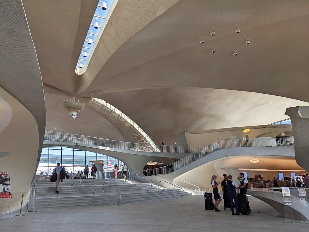 The TWA Hotel lobby in 2022, the former terminal's red-carpeted sunken lounge and curved stairs under the vaulted shell