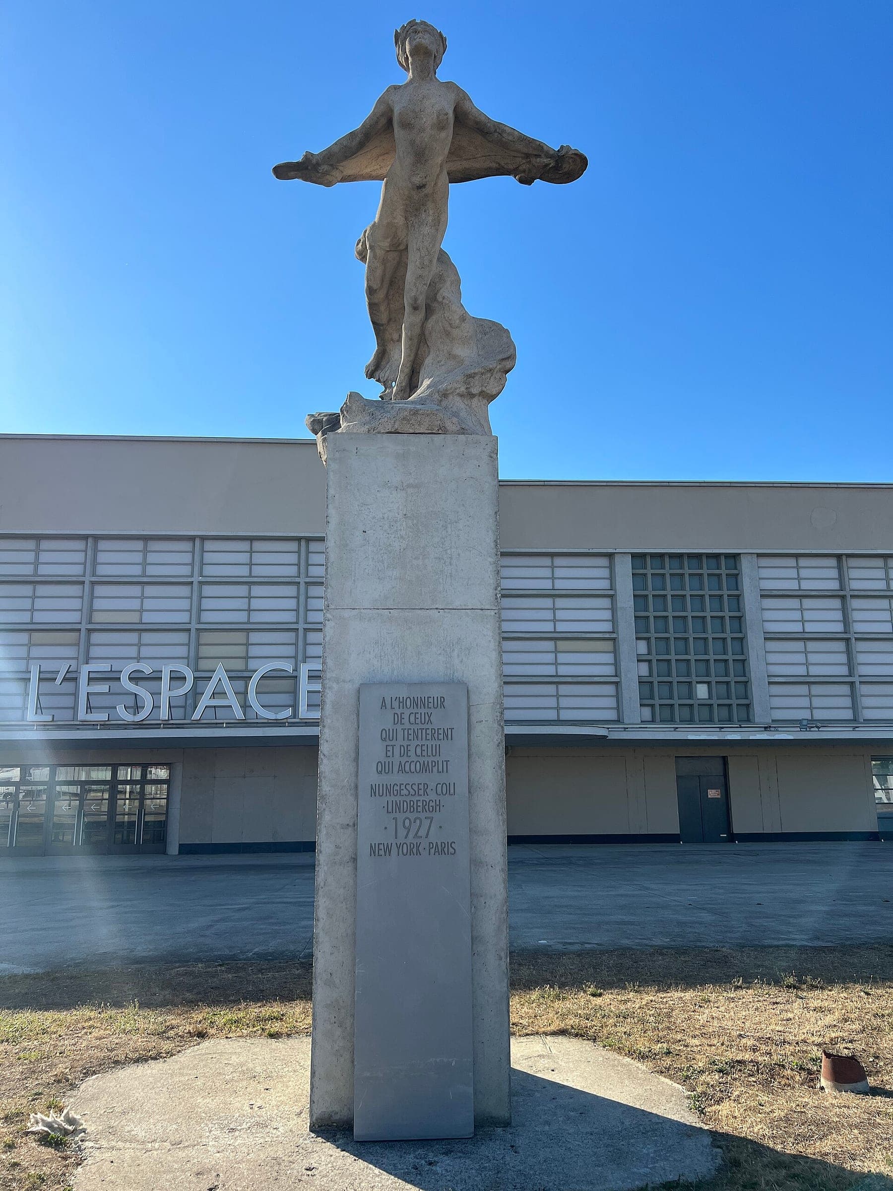 The monument to Nungesser, Coli and Lindbergh: a figure with outstretched arms on a tall stone plinth in front of the museum