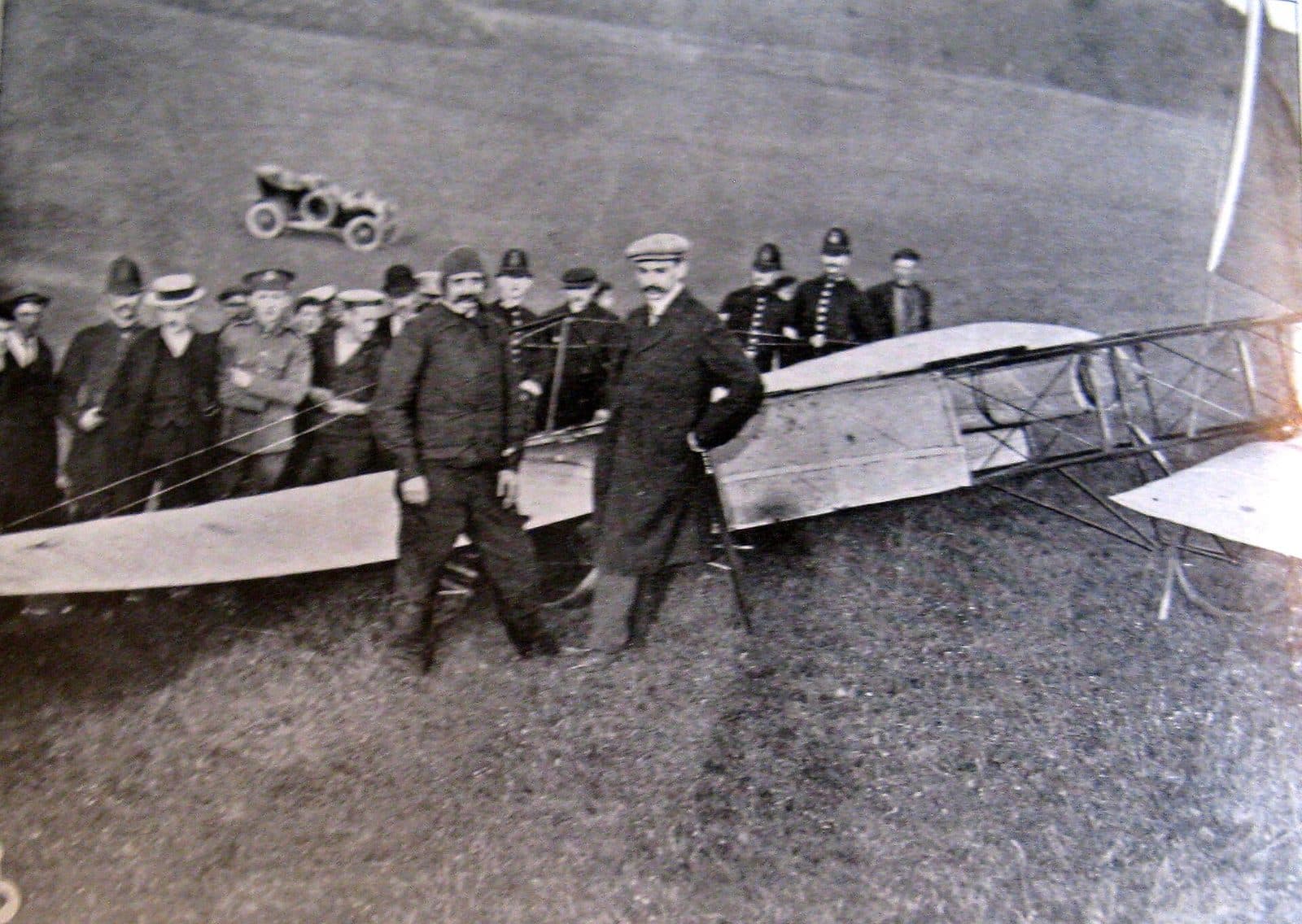 Blériot standing among policemen and spectators beside his damaged monoplane on the meadow at Dover.