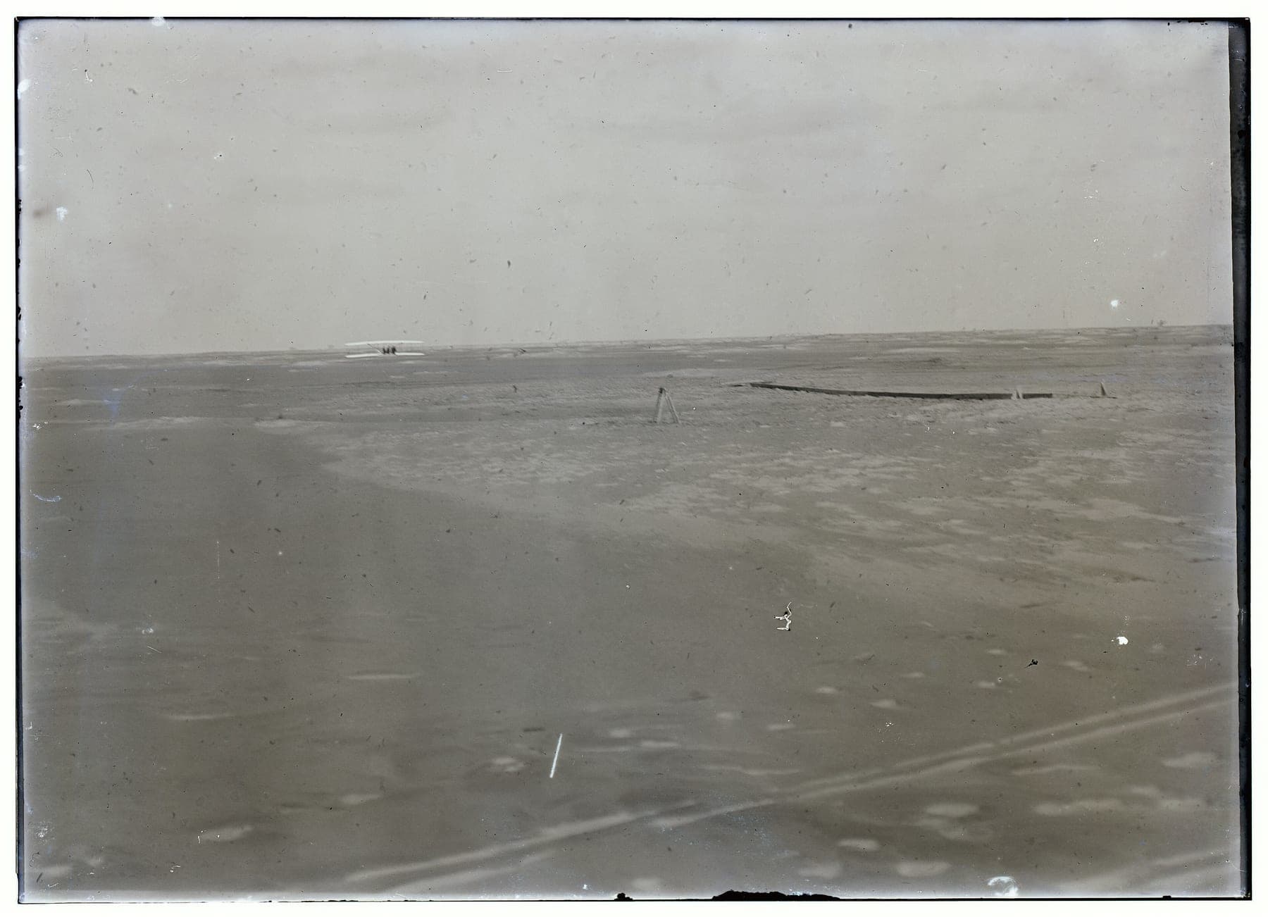 The end of the fourth flight, photographed from the starting point: the machine down in the distance, the wing-rest in the centre and the launching rail at right.