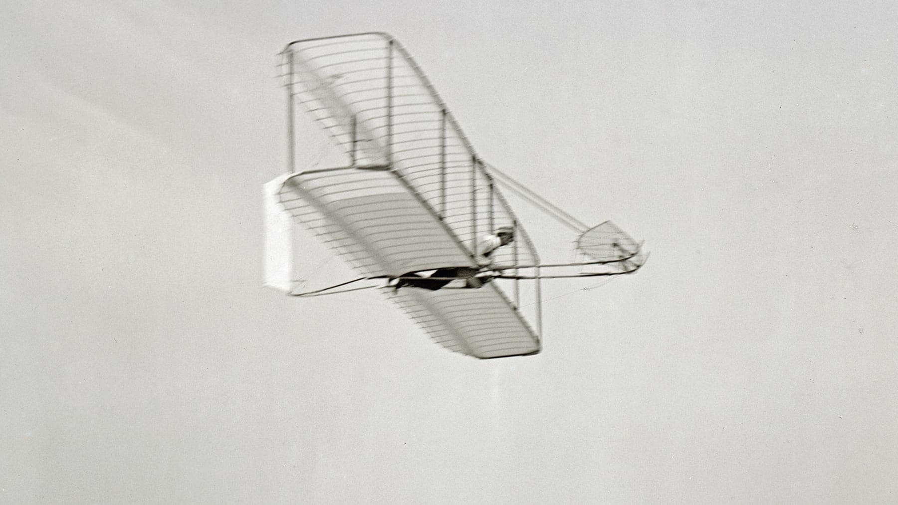 Wilbur Wright gliding to the right in the 1902 machine, seen from below with the movable rear rudder in view.