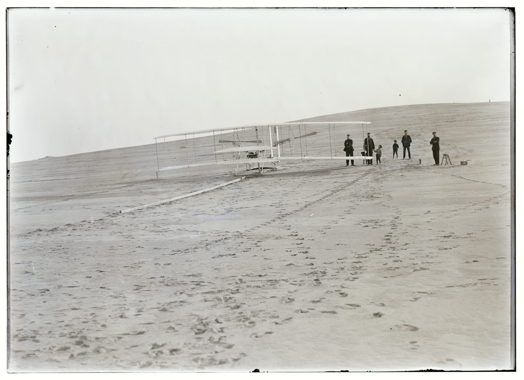 The Flyer on its launching rail at the foot of the big hill on 14 December 1903, with four men from the life-saving station standing by.