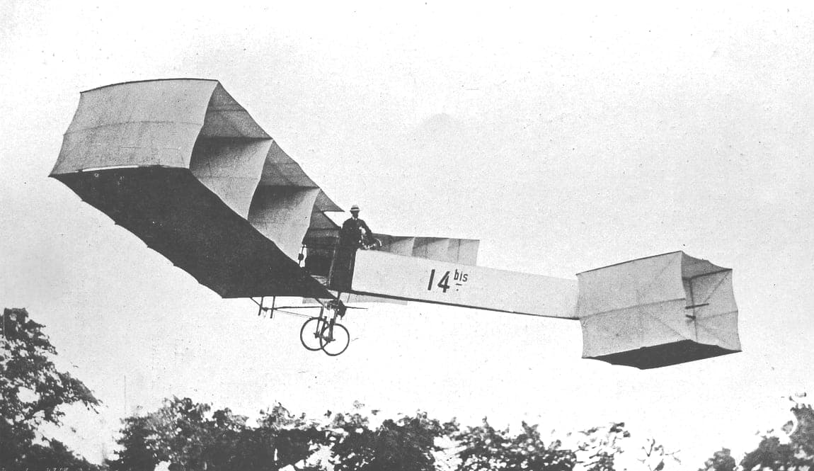 The 14-bis in the air at Bagatelle in 1906, Santos-Dumont standing in the basket between the box-kite cells.