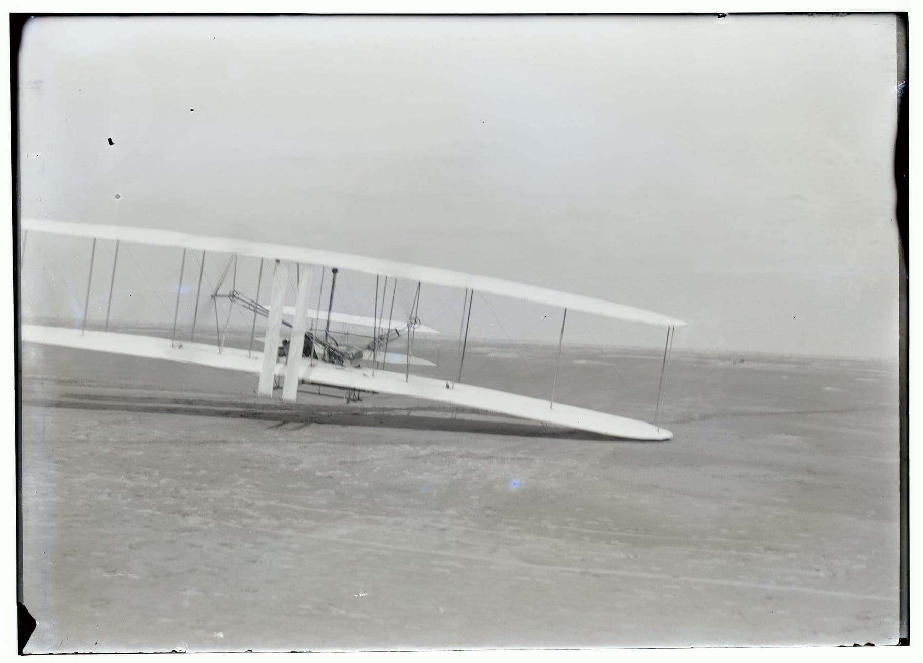 Orville Wright flying the third flight of 17 December 1903, the machine low over the sand.