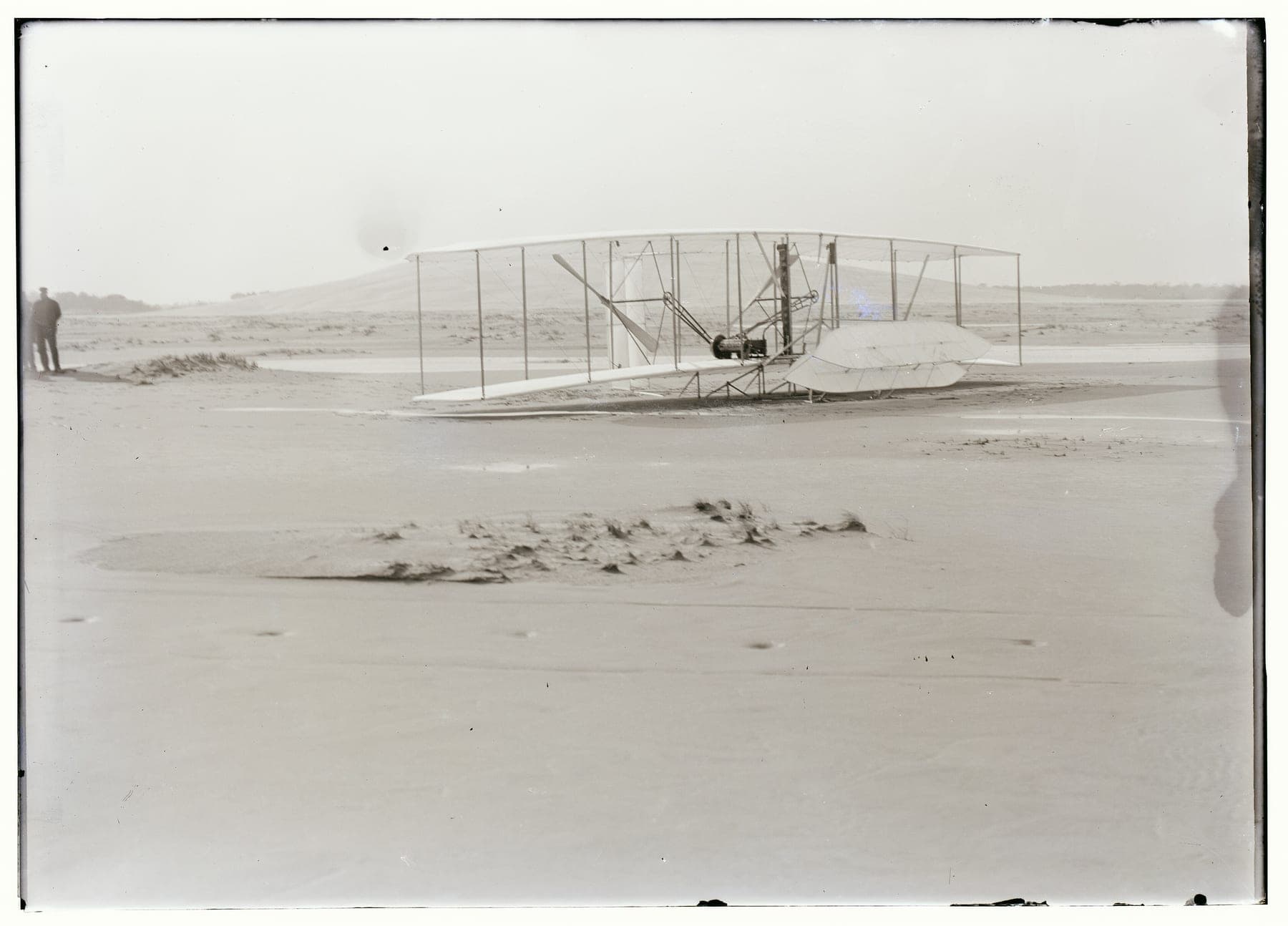 The Flyer on the sand after the gust rolled it over, the elevator frame broken and the wings crumpled.