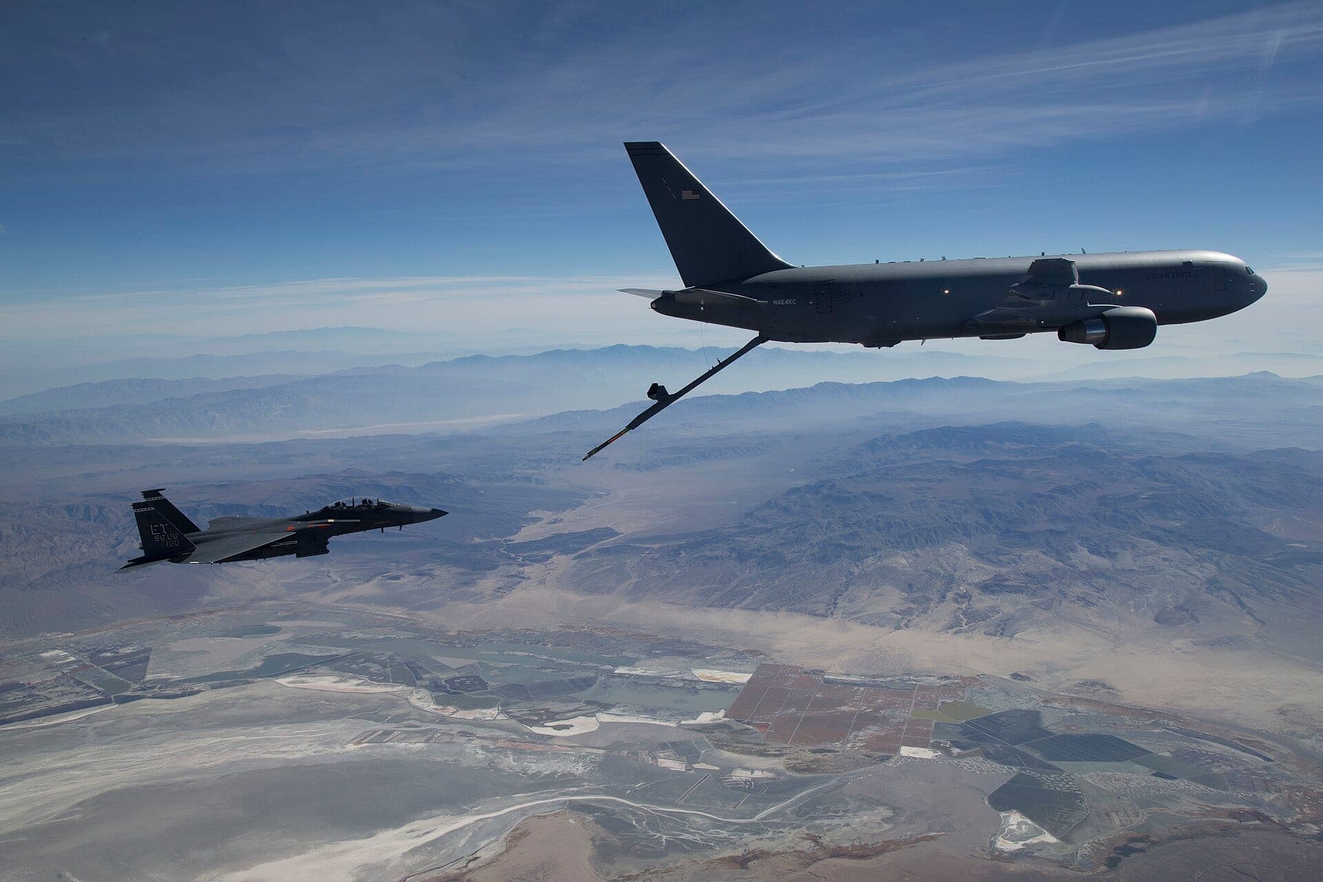 A Boeing KC-46A Pegasus tanker refuelling an F-15 in flight, its boom extended to the receiving aircraft
