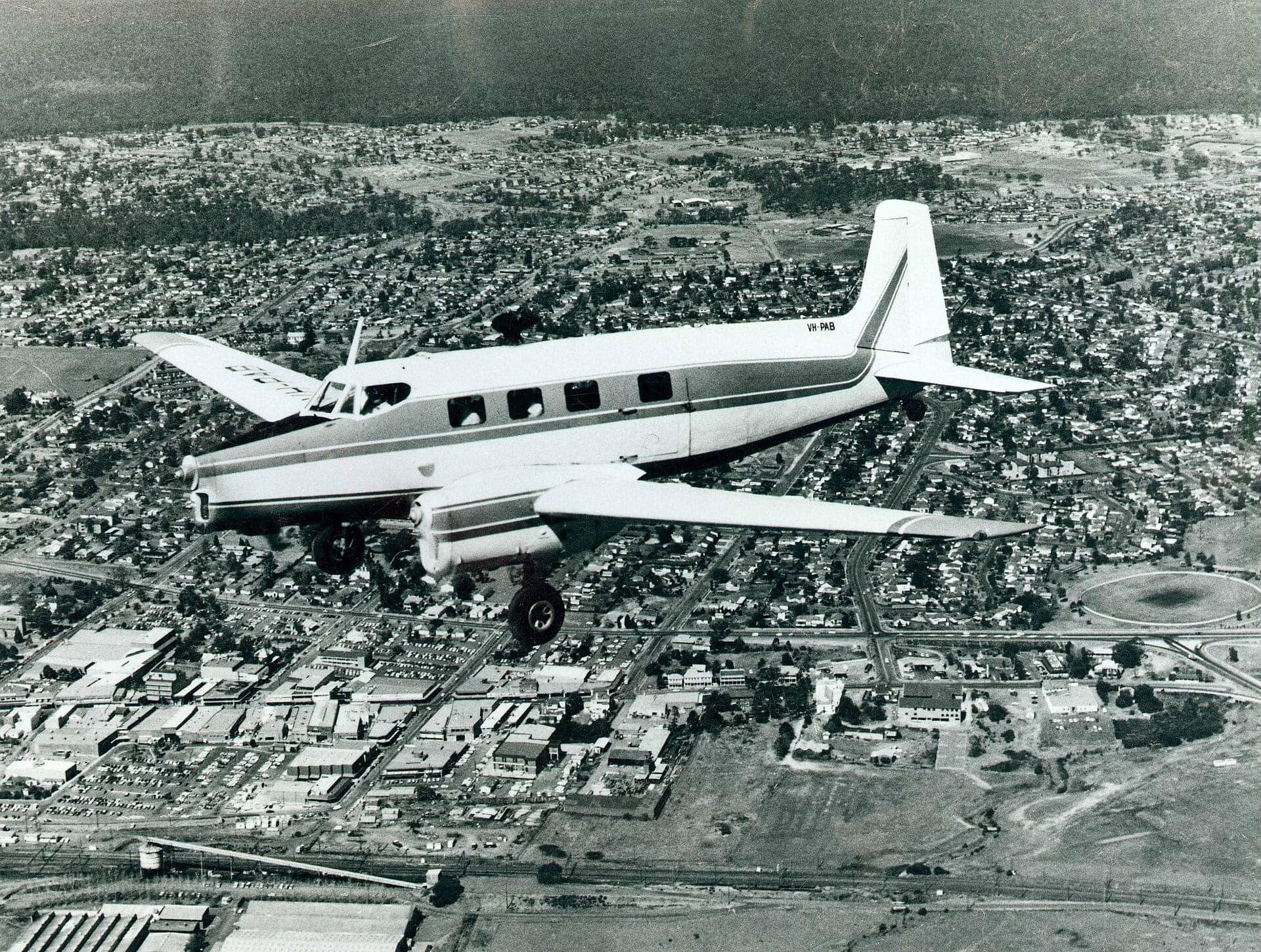 A three-engined de Havilland Australia Drover in flight over a suburban town in New South Wales