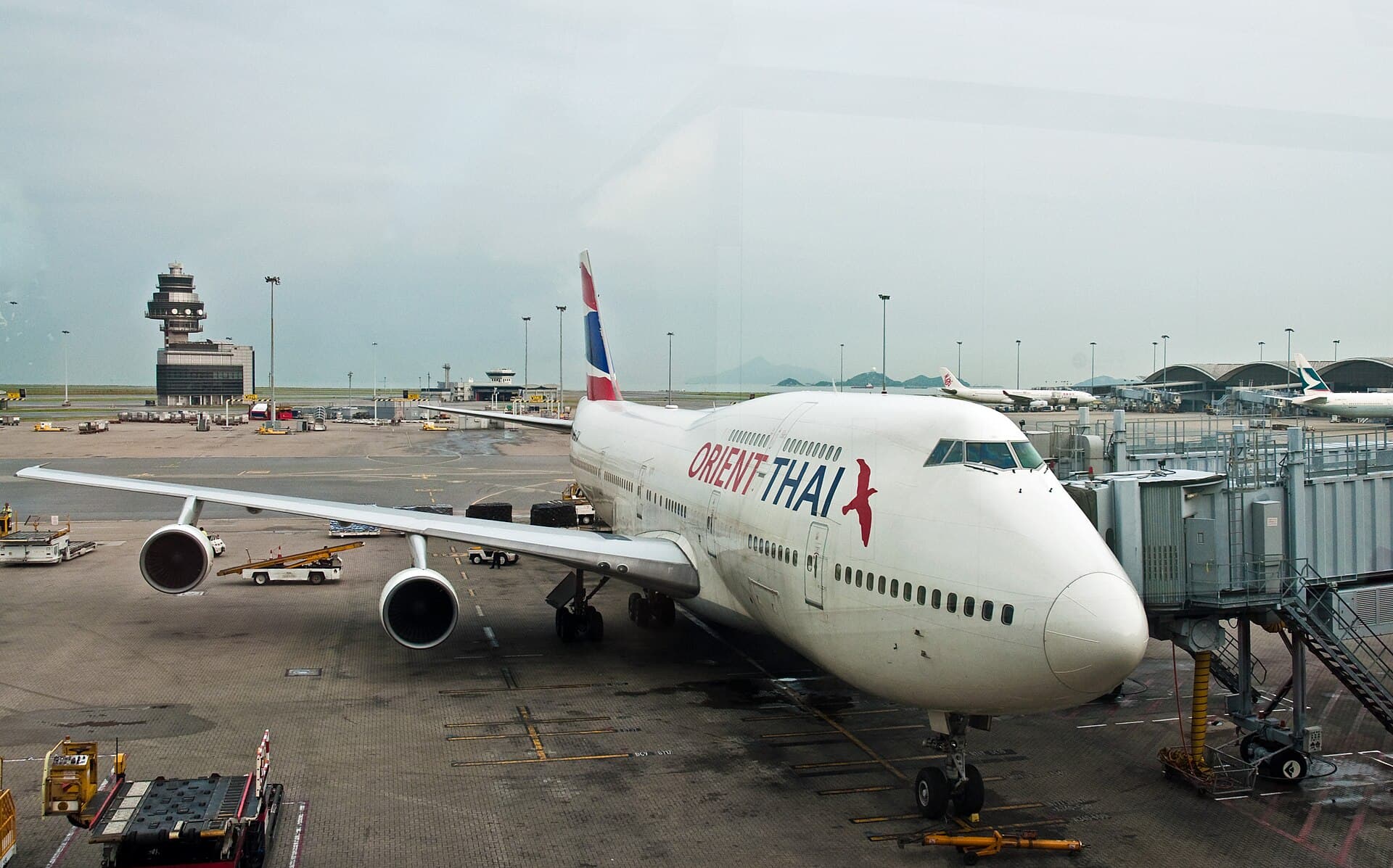 An Orient Thai Boeing 747-300 parked at a jet bridge at Hong Kong International Airport, its stretched upper deck visible along the spine