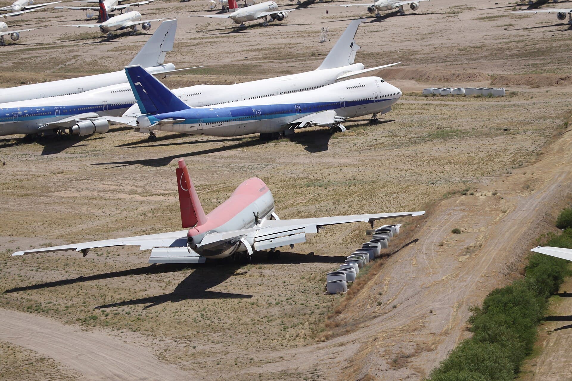 Retired Boeing 747s parked in rows at a desert storage facility, engines covered and paint fading in the sun